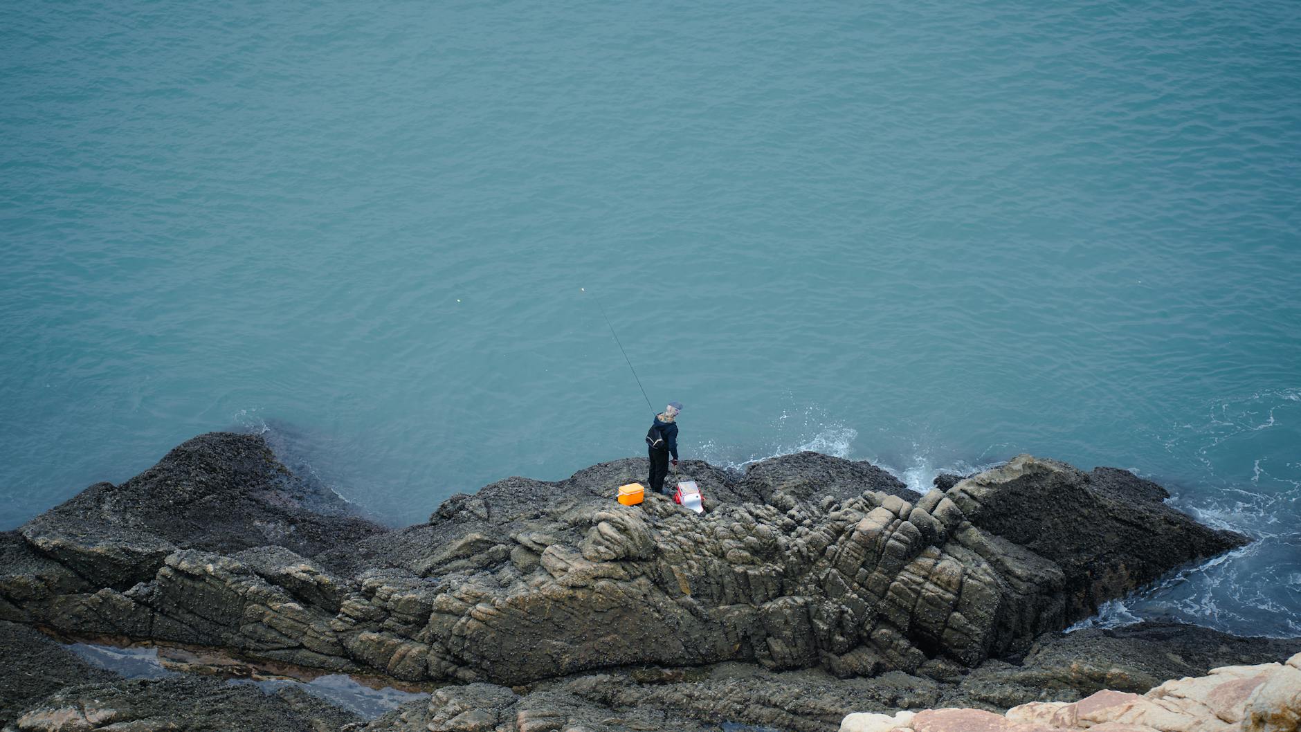 Grecja na ryby z brzegu: proste metody, gatunki i lokalne ograniczenia Wędkarz łowiący z kamienistego brzegu morza w Grecji